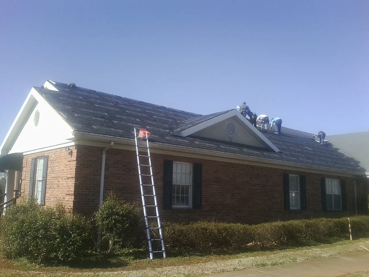 Crew tearing shingles off a brick ranch roof with a ladder set — Emergency Roof Repair work by our crew in Talmage