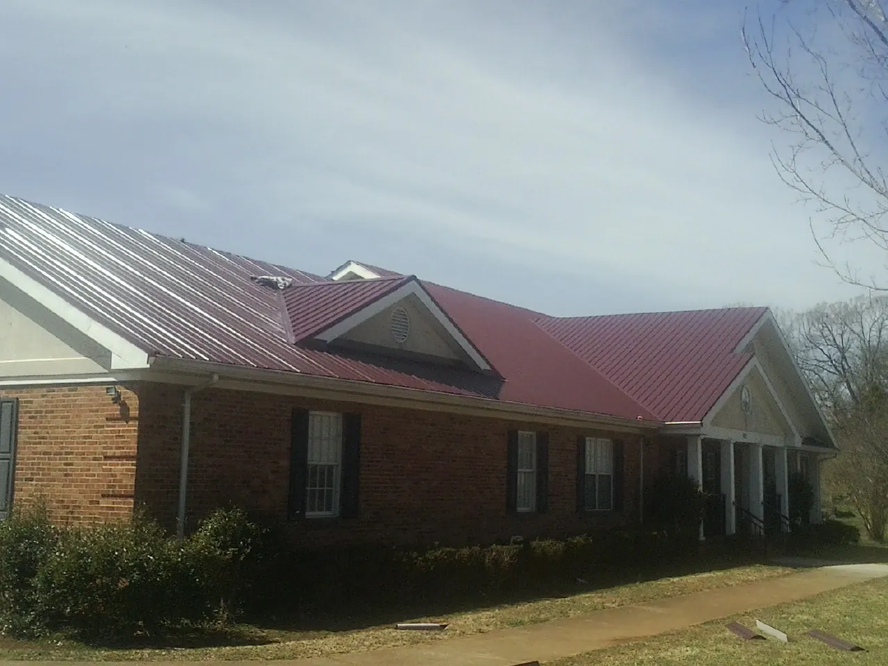 Red metal roof with gabled entries on a long brick building, from a Hail Damage Roof Repair job in Talmage