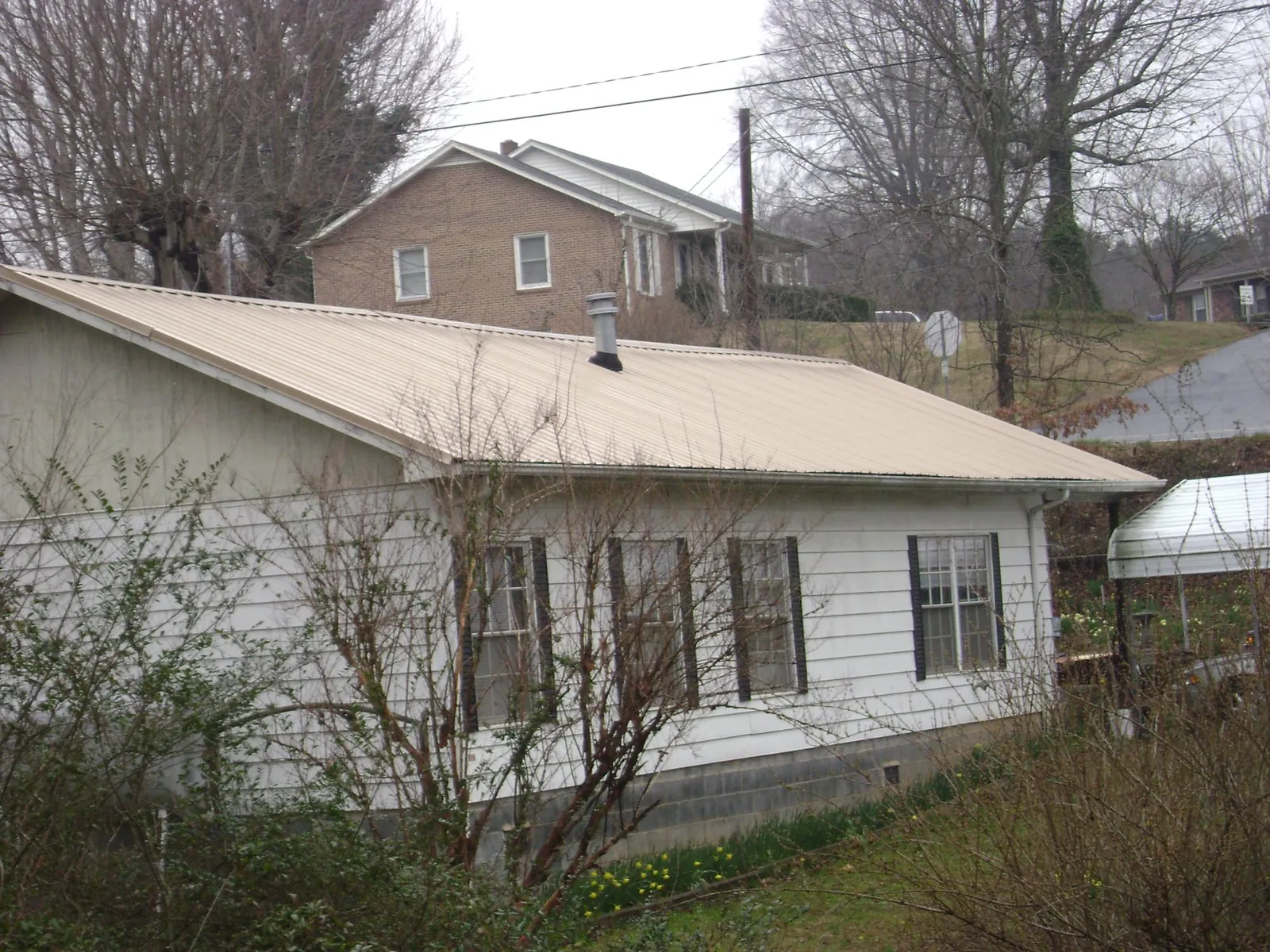Tan metal roof on a white sided house set into a hillside — Commercial Roofing by Roofing Brothers in Talmage