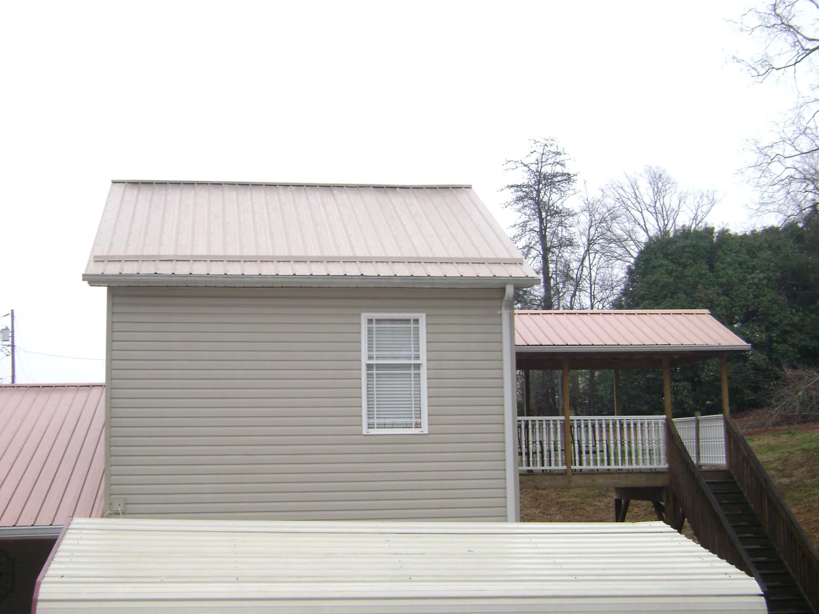 Tan metal roofs on a two story addition and attached porch, from a Roof Replacement job in Talmage
